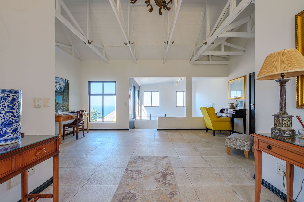 Spacious living area featuring a high vaulted ceiling with exposed trusses, tiled flooring, and large windows offering natural light and coastal views.