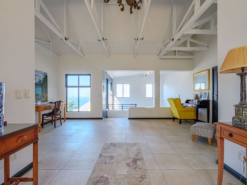 Spacious living area featuring a high vaulted ceiling with exposed trusses, tiled flooring, and large windows offering natural light and coastal views.
