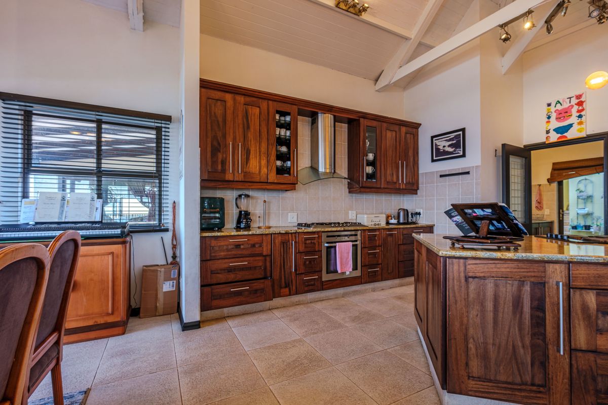 A well-appointed kitchen featuring rich wooden cabinetry, granite countertops, stainless steel appliances, and a high vaulted ceiling with exposed beams.