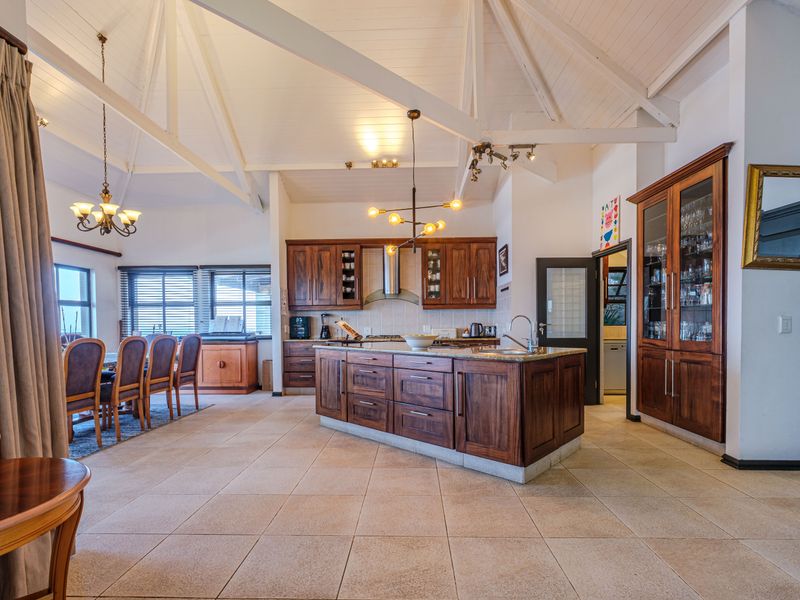 Spacious open-plan kitchen and dining area featuring vaulted ceilings with exposed trusses, custom timber cabinetry, a central island, and neutral tiled flooring.