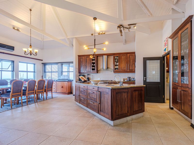 Spacious open-plan kitchen and dining area featuring vaulted ceilings with exposed beams, rich timber cabinetry, granite countertops, and large windows with natural light.