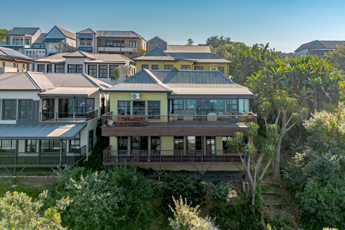 An elevated rear view of a multi-level residential property featuring extensive timber decking, large glass doors, and a corrugated metal roof.