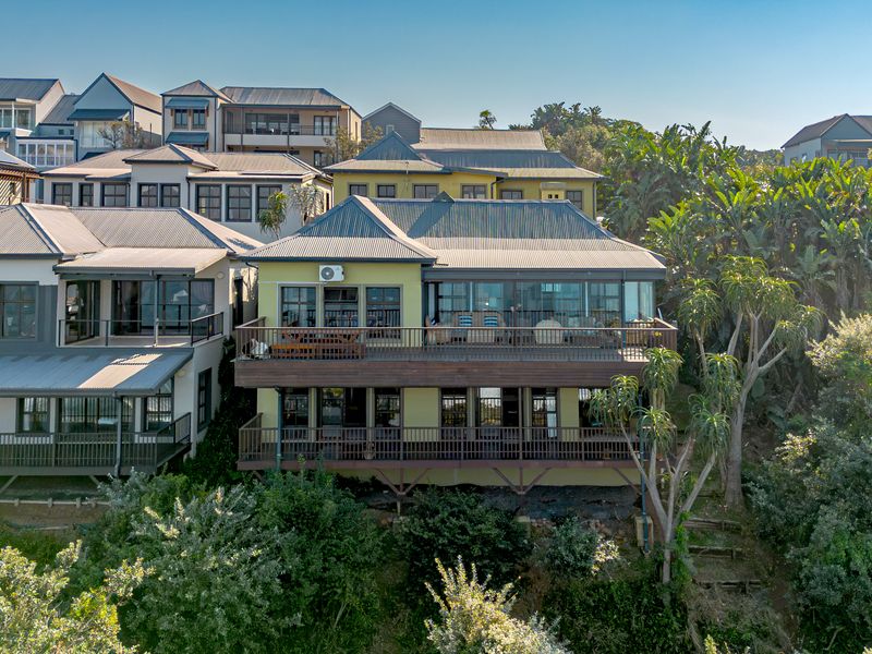 An elevated rear view of a multi-level residential property featuring extensive timber decking, large glass doors, and a corrugated metal roof.