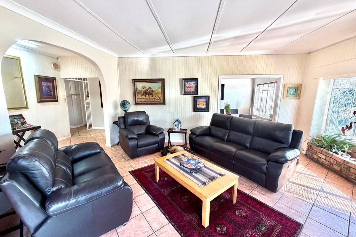 A spacious living room featuring tiled flooring, decorative wall panelling, and an arched entryway leading to adjacent living areas.
