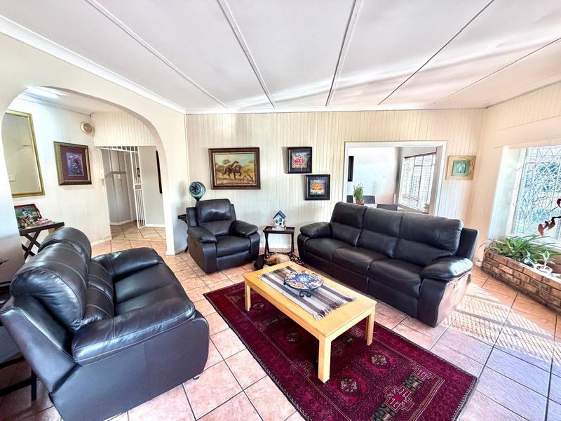 A spacious living room featuring tiled flooring, decorative wall panelling, and an arched entryway leading to adjacent living areas.