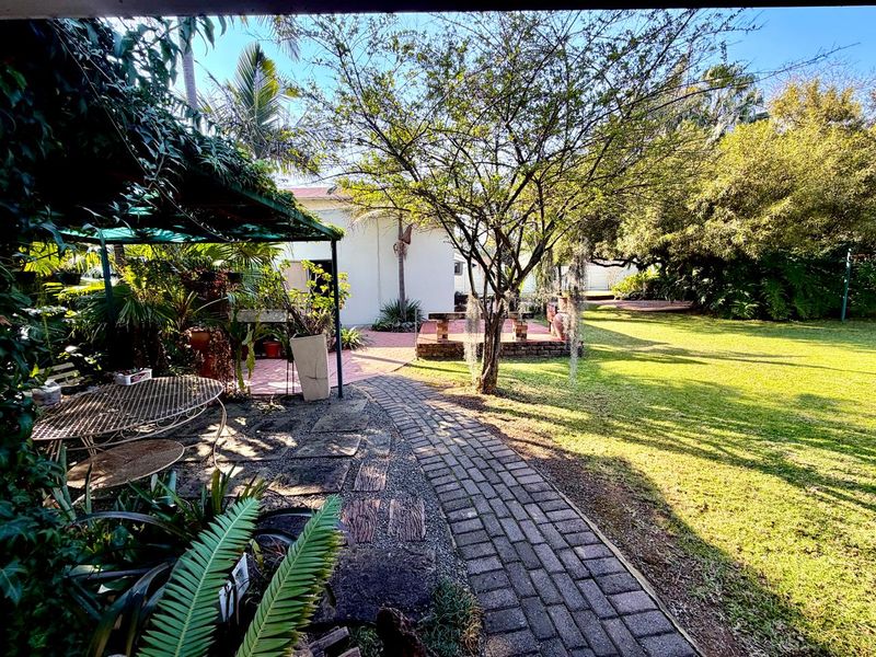 A spacious rear garden featuring a brick paved pathway, a covered patio area, and a brick-built seating feature set within a landscaped lawn.