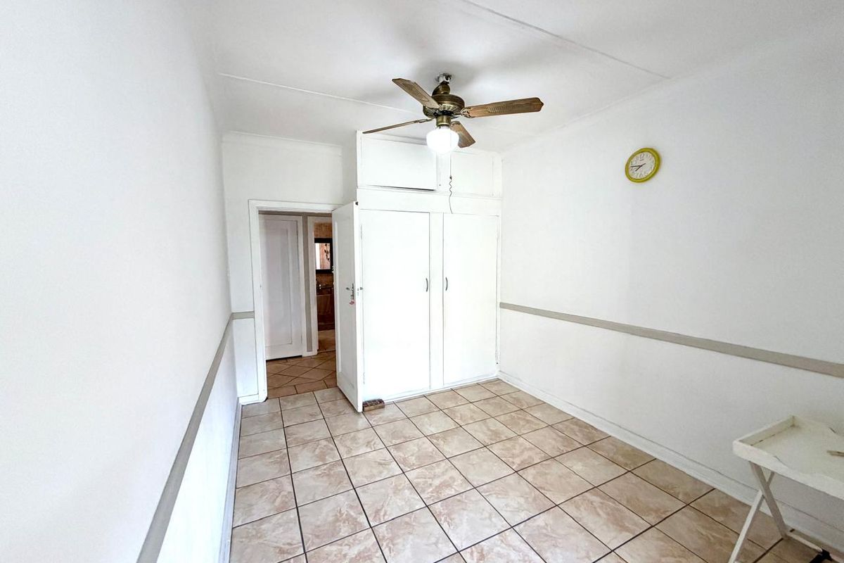 A vacant bedroom featuring tiled flooring, built-in cupboards with overhead storage, and a ceiling fan, offering a blank canvas for renovation.