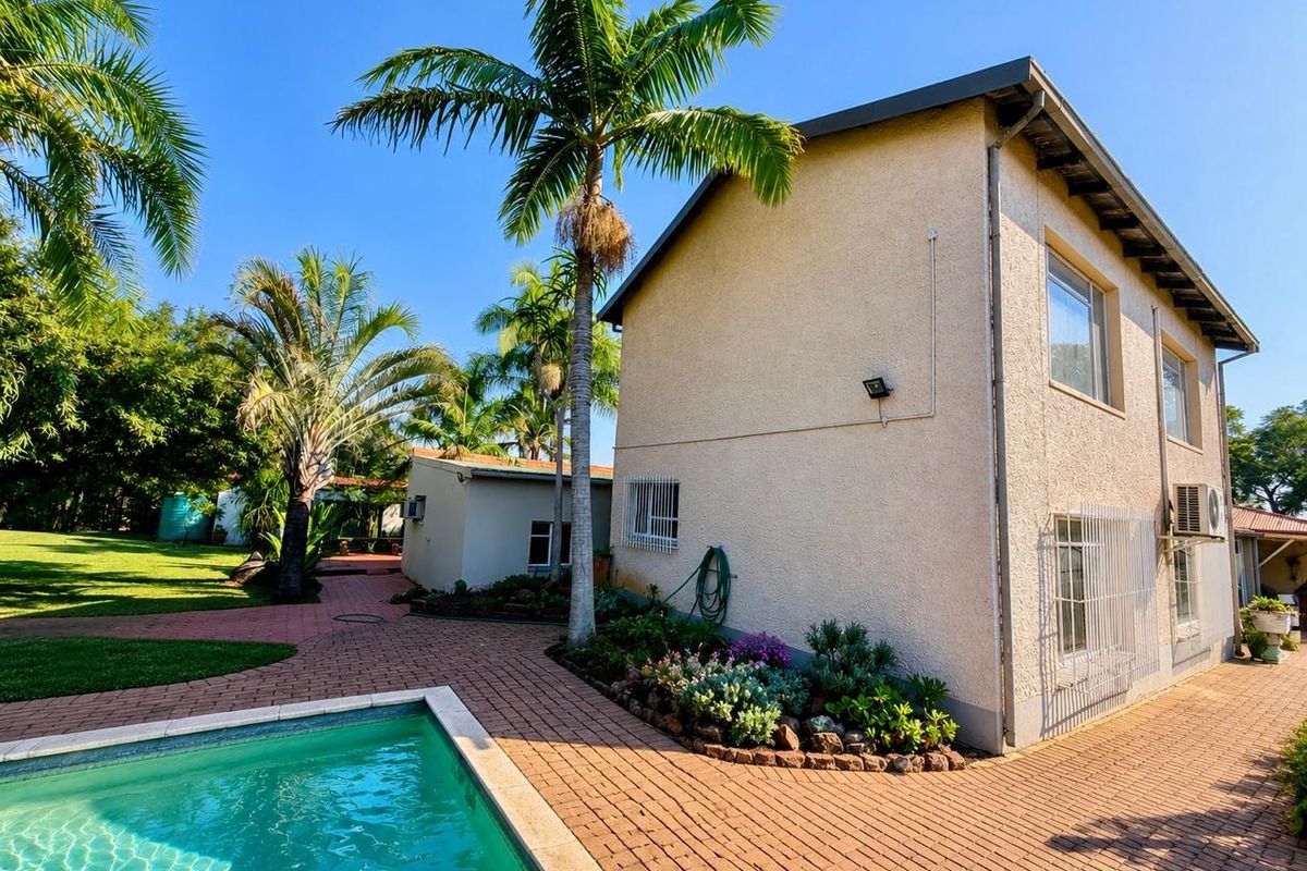 Rear exterior view featuring a swimming pool, paved patio area, and landscaped garden surrounding the main house structure.