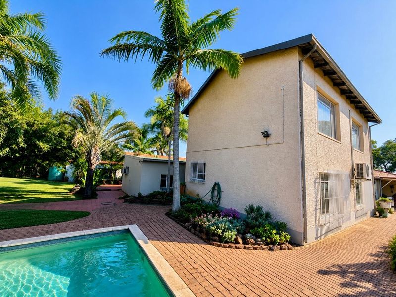 Rear exterior view featuring a swimming pool, paved patio area, and landscaped garden surrounding the main house structure.