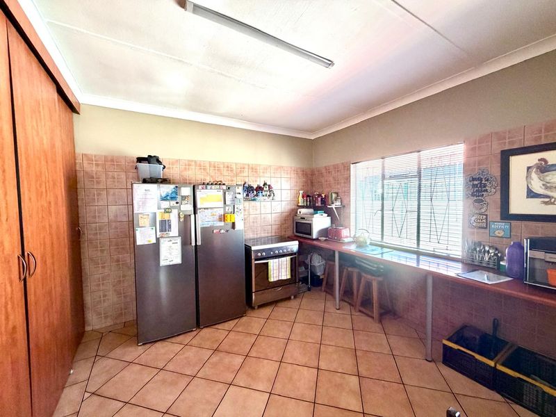 Functional kitchen featuring tiled flooring, tiled splashbacks, built-in cabinetry, and a freestanding stove with natural light from a window with security bars.