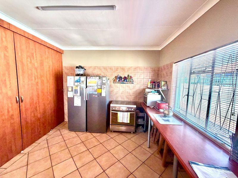 A functional kitchen featuring tiled flooring, a tiled splashback, built-in cabinetry, and a freestanding stove with natural light from the side window.