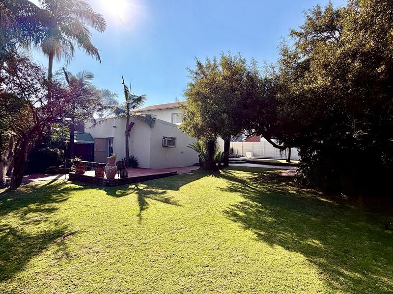 A spacious rear garden featuring a well-maintained lawn, mature trees, and a brick patio area attached to the rear elevation of the house.