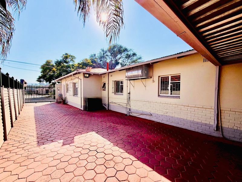 Rear exterior view of the property featuring a paved driveway, covered patio area, and solar geyser installation.