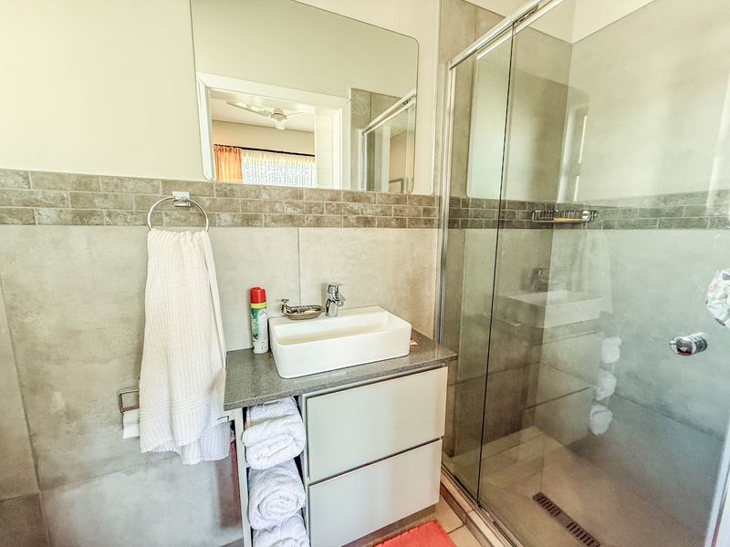 A modern bathroom featuring a vessel sink on a stone vanity, a glass-enclosed shower, and neutral wall tiling.