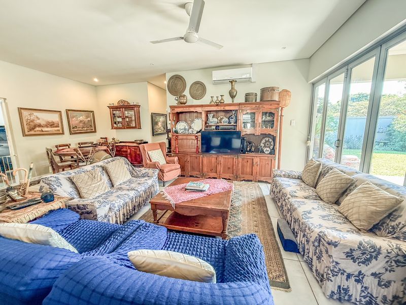 Spacious living room featuring tiled flooring, ceiling fan, split-system air conditioning, and large aluminium sliding doors providing access to the garden.