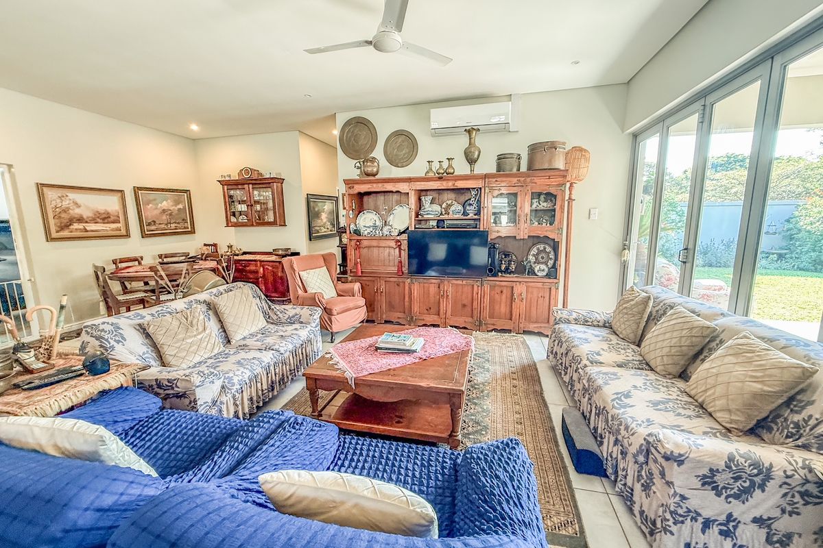 Spacious living room featuring tiled flooring, ceiling fan, split-system air conditioning, and large aluminium sliding doors providing access to the garden.