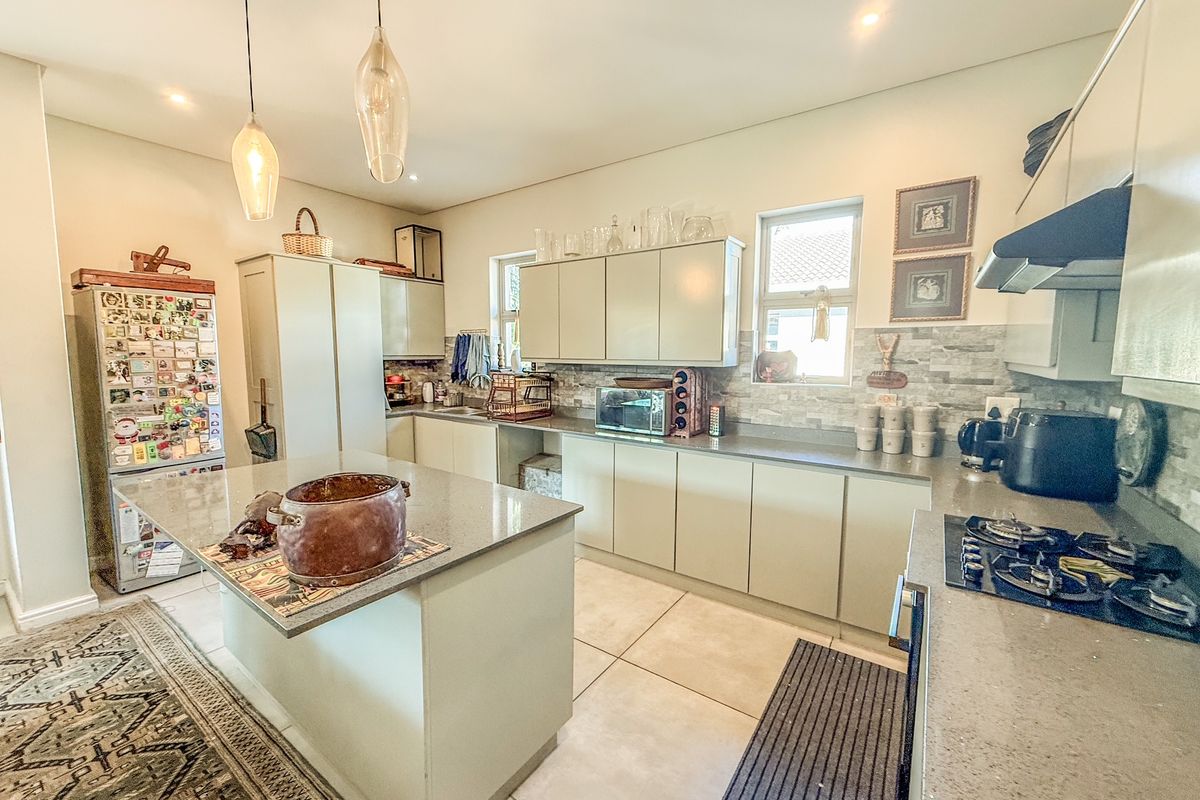 Modern kitchen featuring a central island with stone countertops, ample built-in cabinetry, gas hob, extractor fan, and stylish pendant lighting.