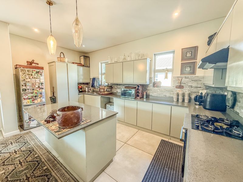 Modern kitchen featuring a central island with stone countertops, ample built-in cabinetry, gas hob, extractor fan, and stylish pendant lighting.