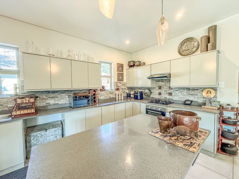 A well-maintained kitchen featuring stone countertops, a central island, built-in oven, gas hob, and modern cabinetry with a decorative tiled backsplash.
