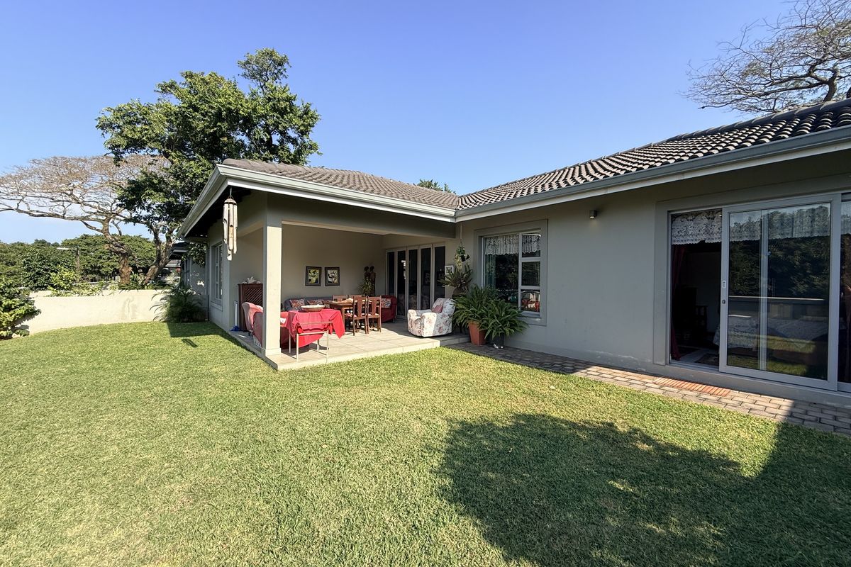 A well-maintained rear exterior view of the townhouse featuring a covered patio, paved walkway, and a spacious private lawn area.