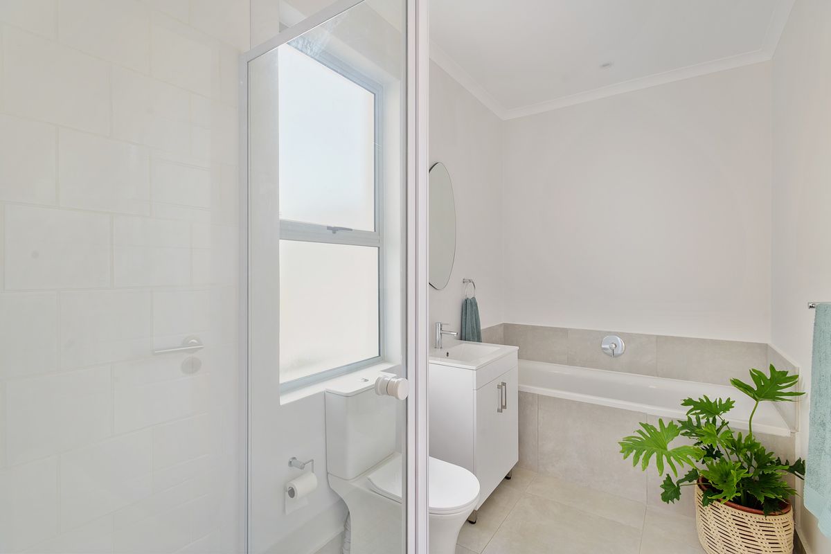 A clean, modern bathroom featuring a built-in bathtub, a vanity with basin, a toilet, and a separate shower enclosure with neutral tiling.