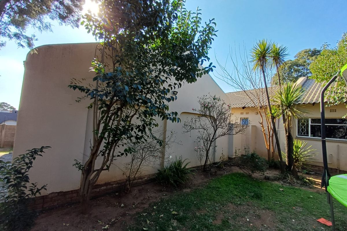 A view of the rear exterior of the house featuring plastered walls, a tiled roof, and established garden landscaping.