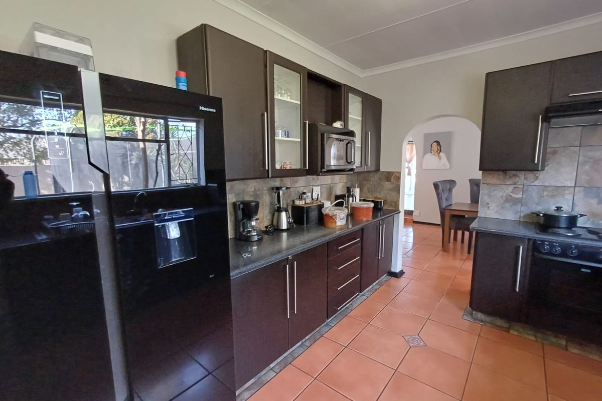 A functional kitchen featuring dark wood cabinetry, stone tile backsplash, built-in appliances, and ceramic floor tiles, with an arched doorway leading to the dining area.