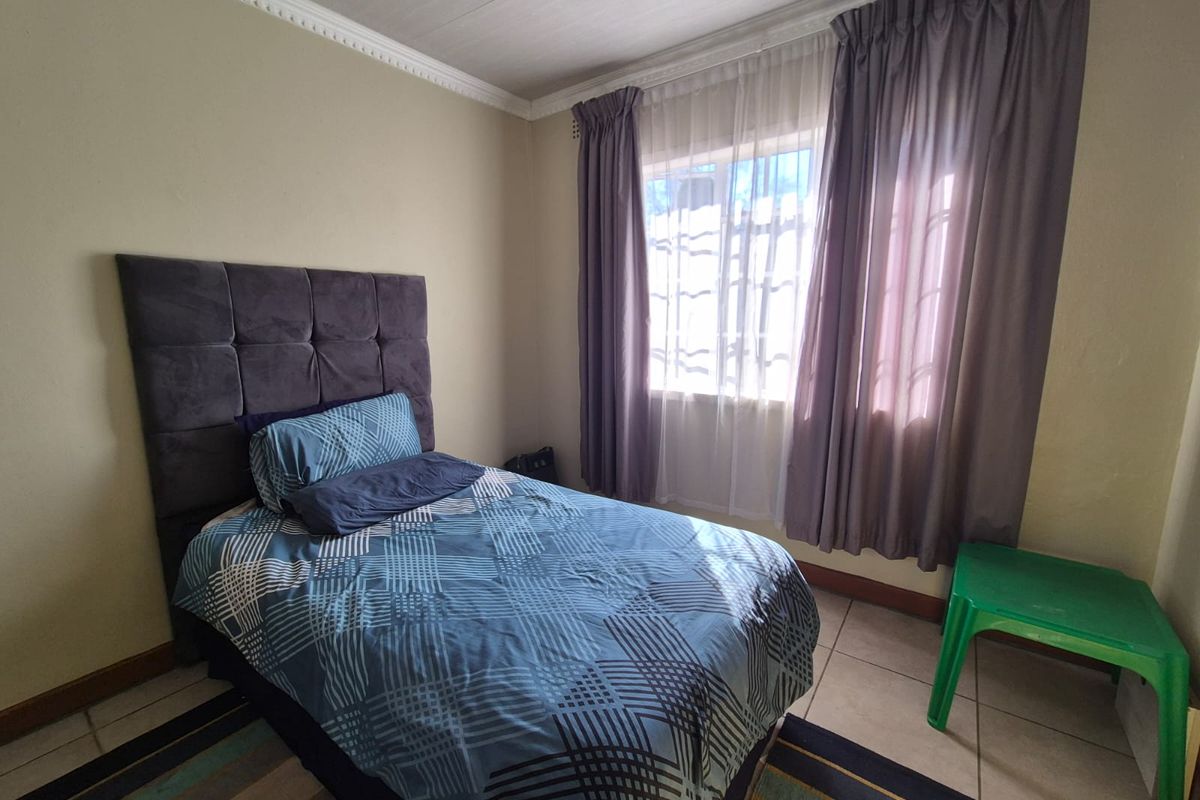 A functional bedroom featuring tiled flooring, ceiling cornice detailing, and a window fitted with security bars.