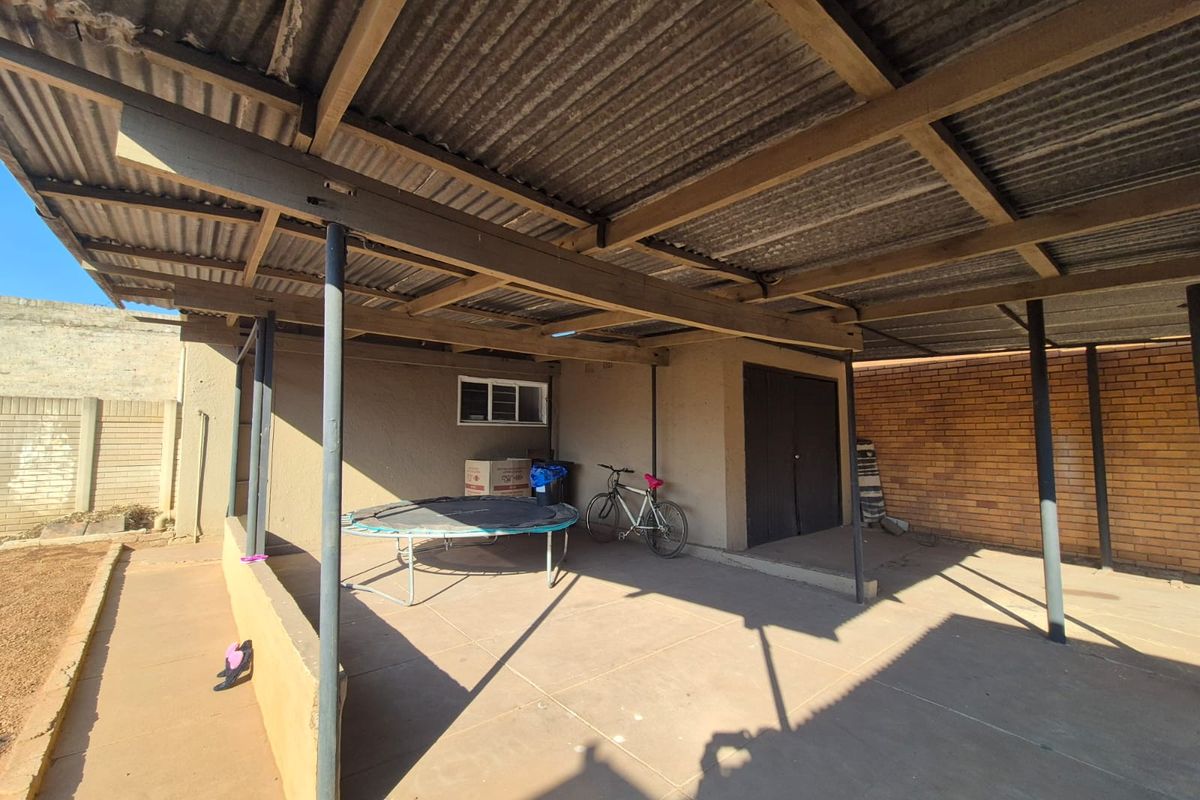 A covered outdoor patio area featuring a corrugated iron roof, steel support columns, and concrete flooring, suitable for an entertainment or utility space.