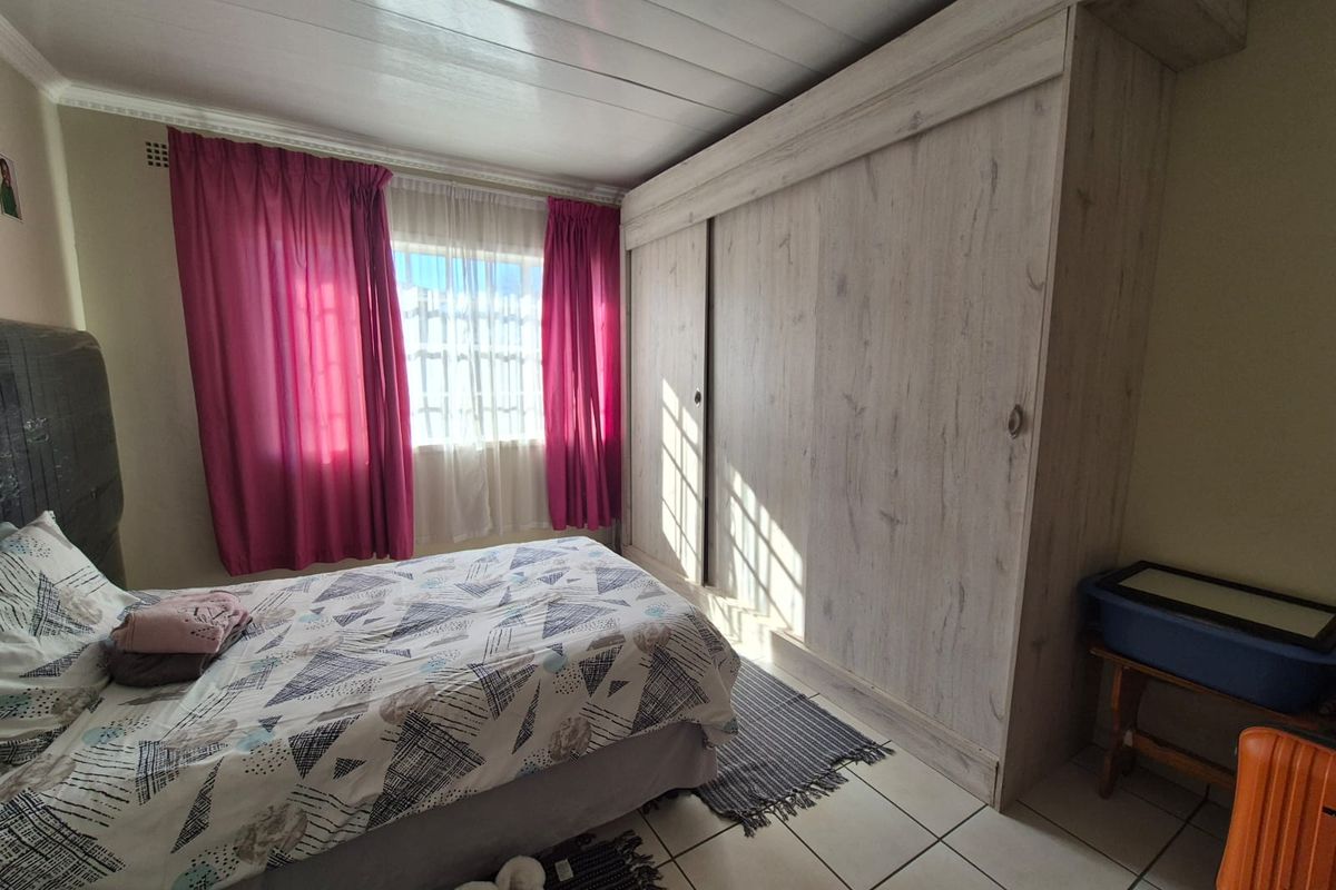A functional bedroom featuring a large built-in wardrobe, tiled flooring, and a panelled ceiling, offering a practical layout for comfortable living.