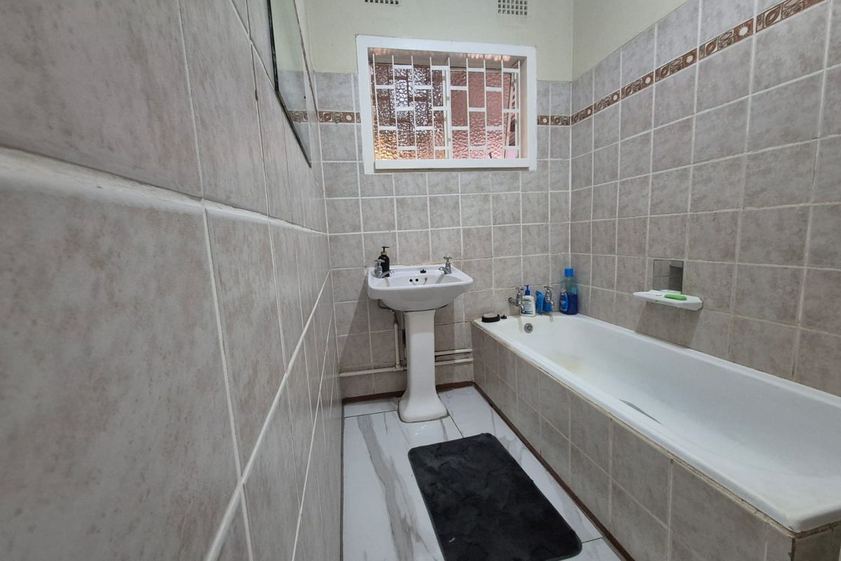 A functional bathroom featuring a pedestal basin, built-in bathtub, and neutral ceramic wall tiling with marble-effect floor tiles.