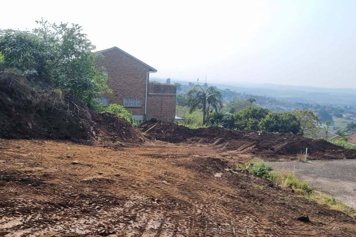 A view of a cleared, sloped residential plot showing earthworks and surrounding neighborhood landscape.