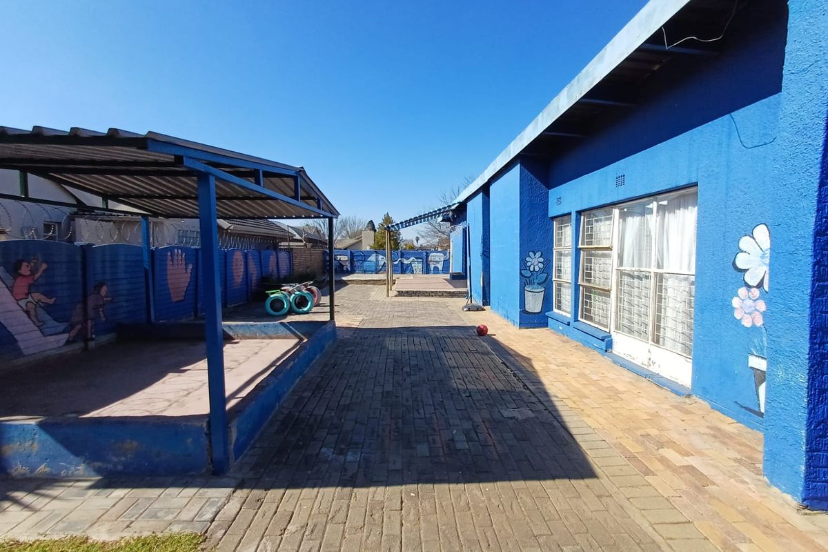 A paved rear courtyard area featuring a covered play structure, enclosed by painted brick boundary walls with security fencing.
