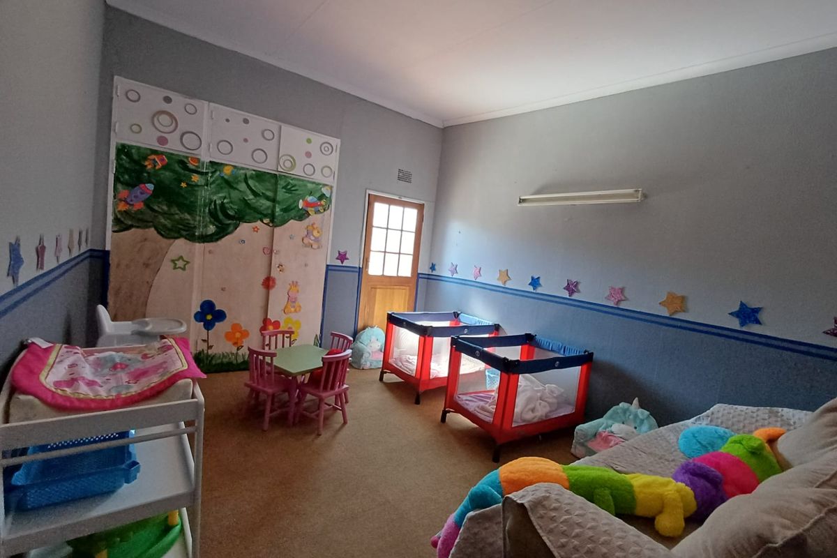 A spacious bedroom featuring built-in cupboards, carpeted flooring, and a timber door, currently utilized as a nursery space.