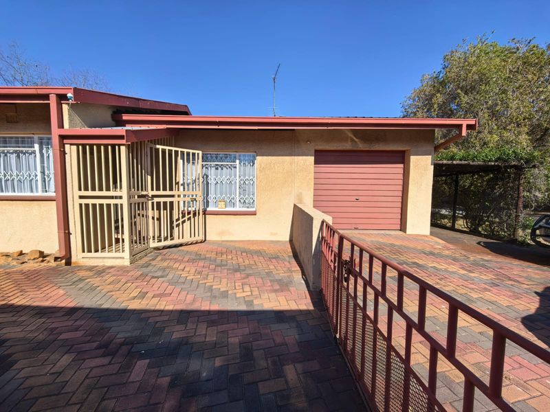 Front exterior view of the property featuring a paved driveway, single garage, and secure gated entrance with security bars on windows.