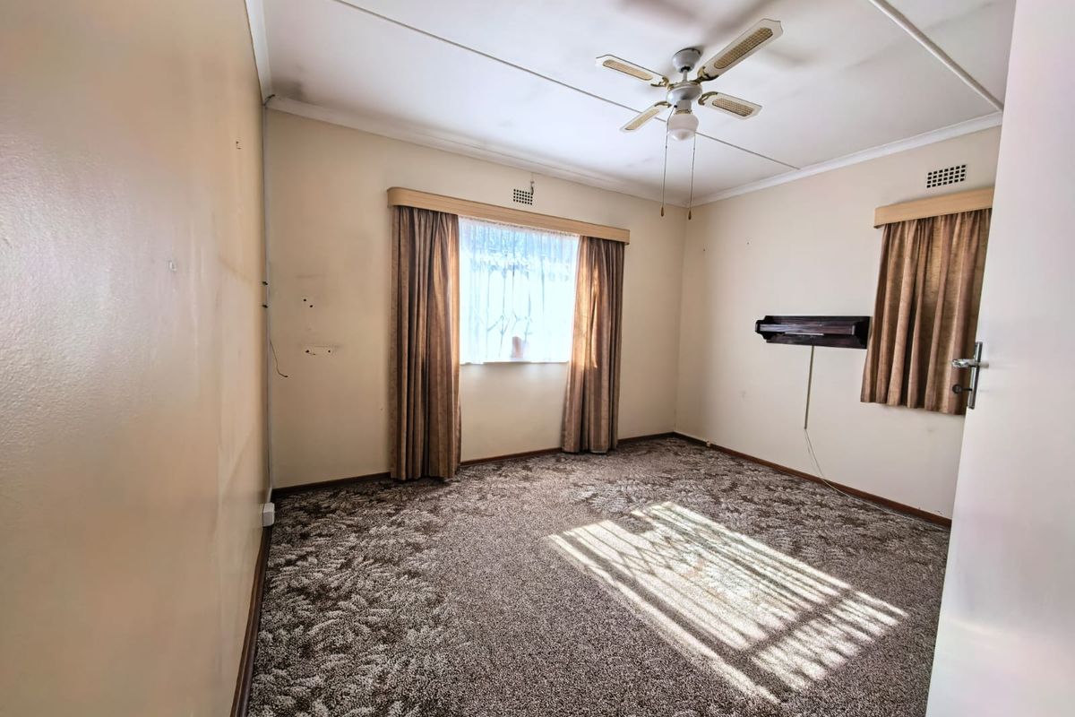 A spacious, empty bedroom featuring carpeted flooring, a ceiling fan, and dual windows with existing curtain rails.