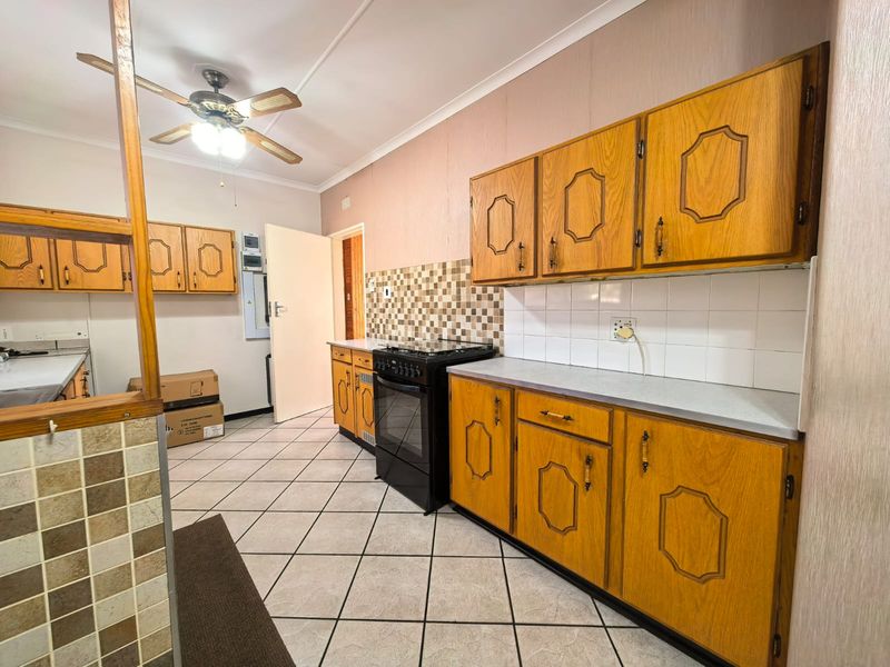 A functional kitchen featuring traditional wooden cabinetry, tiled backsplash, and tiled flooring, offering a dated aesthetic ready for modernization.