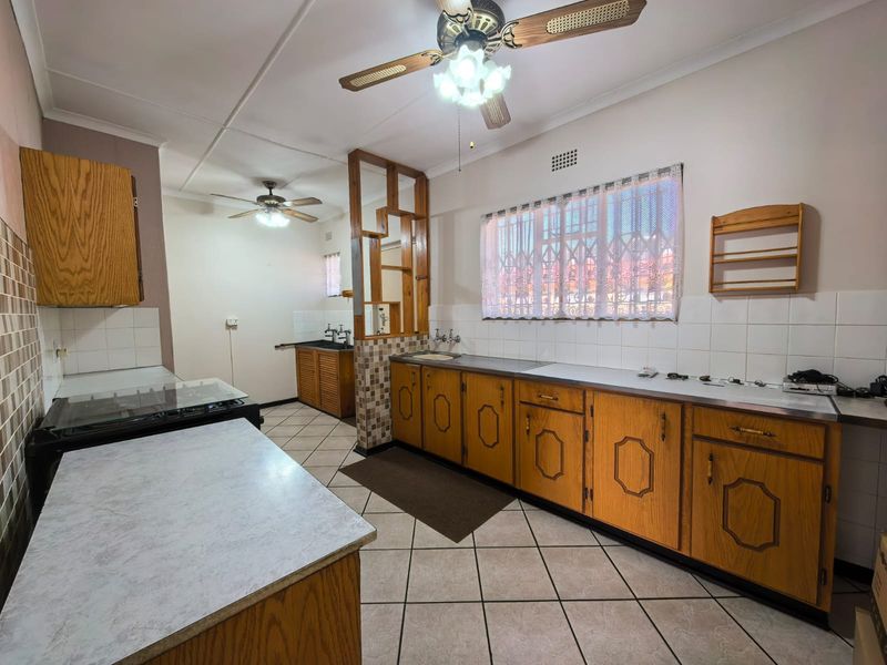 Spacious kitchen featuring extensive wooden cabinetry, laminate countertops, tiled splashbacks, and dual ceiling fans, offering a functional layout with potential for modern updates.
