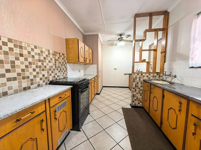 A functional kitchen featuring wooden cabinetry, tiled backsplash, a freestanding stove, and a unique timber room divider, offering potential for modern updates.