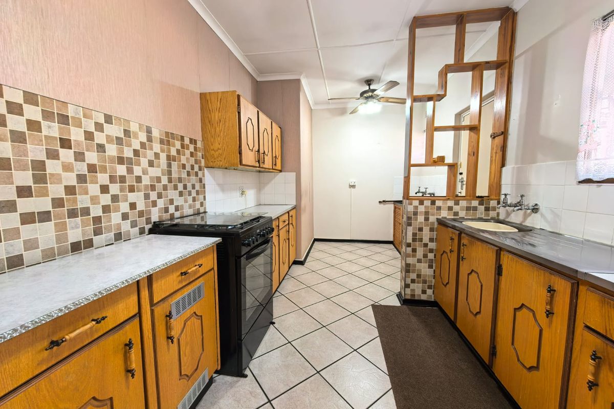 A functional kitchen featuring wooden cabinetry, tiled backsplash, a freestanding stove, and a unique timber room divider, offering potential for modern updates.