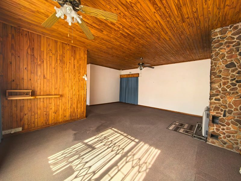 Spacious living room featuring a prominent stone fireplace, timber-clad ceiling, and wood-paneled accent wall, offering a blank canvas for modern renovation.