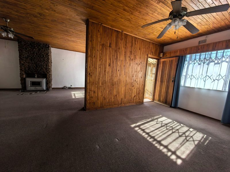 Spacious living area featuring wood-paneled walls, a timber ceiling, and a prominent stone fireplace with a built-in insert.