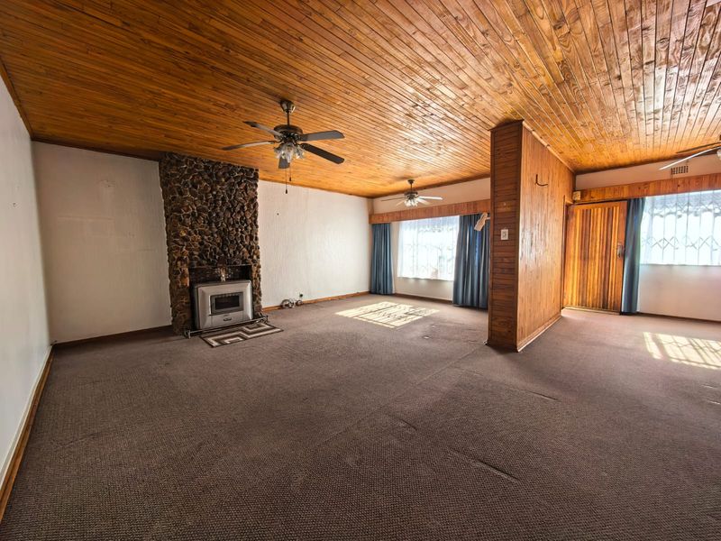 Spacious living room featuring a stone fireplace with a wood-burning stove, timber-clad ceiling, and ceiling fans, offering a dated but functional layout.
