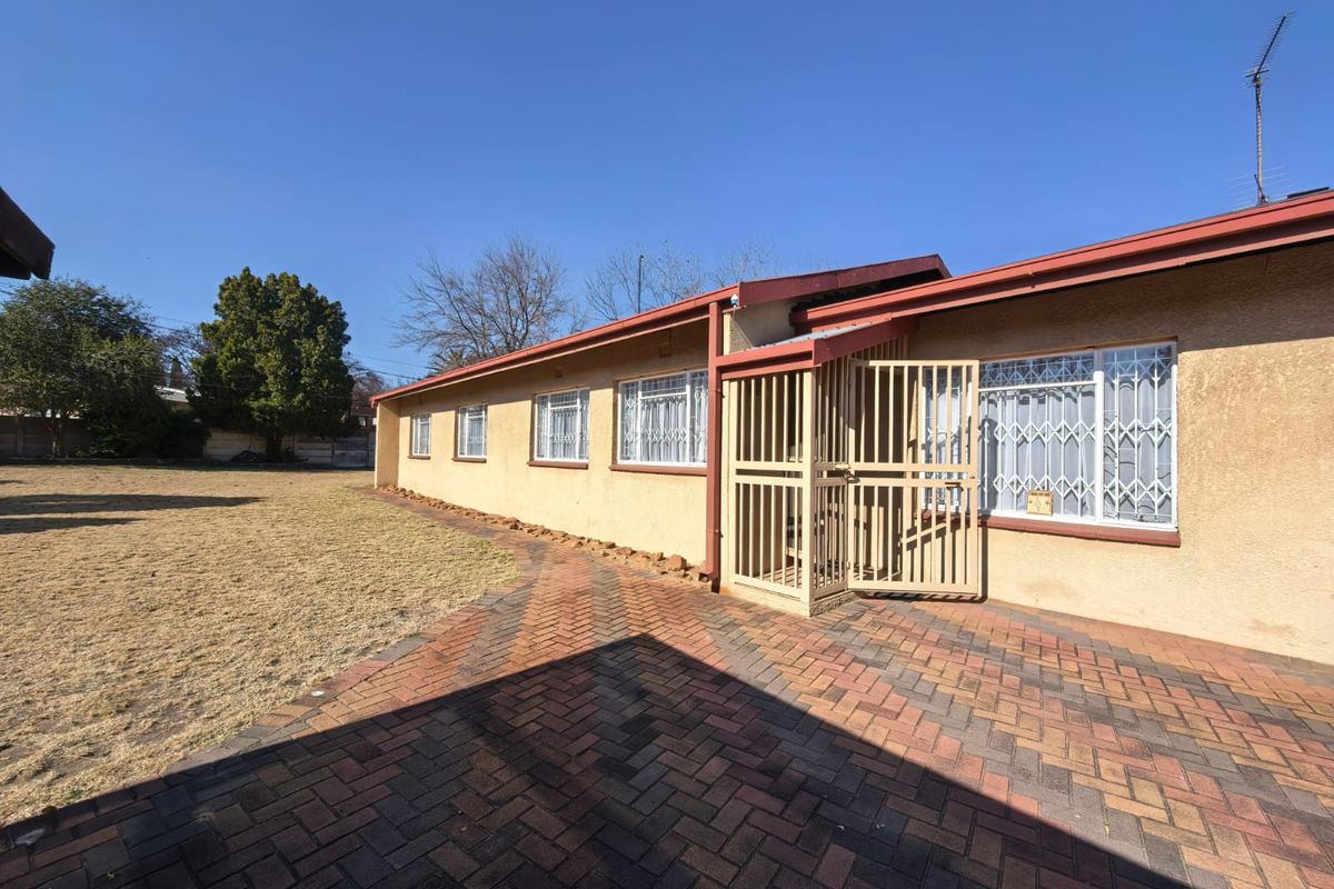 Rear view of the property featuring a brick paved patio area, security gates, and metal roofing with access to the backyard.