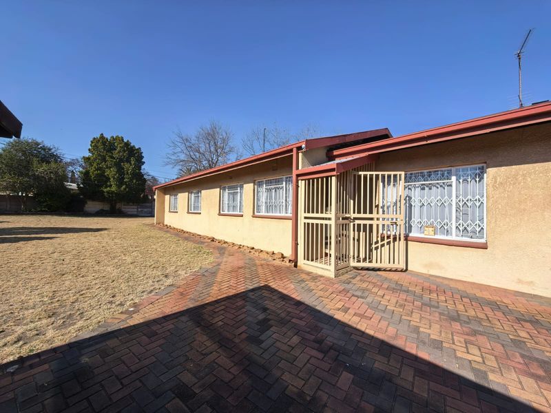 Rear view of the property featuring a brick paved patio area, security gates, and metal roofing with access to the backyard.