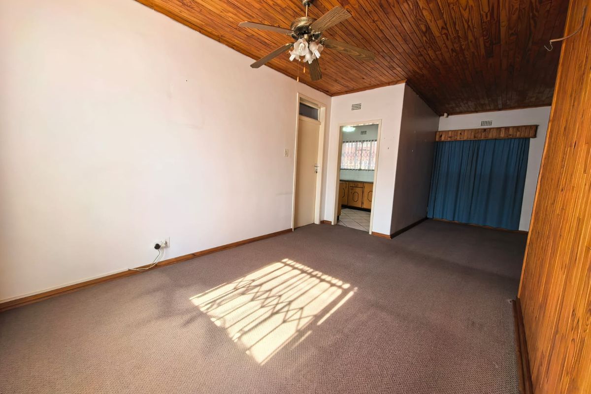Spacious living area featuring timber ceiling paneling, a ceiling fan, and carpeted flooring, offering a blank canvas for renovation.