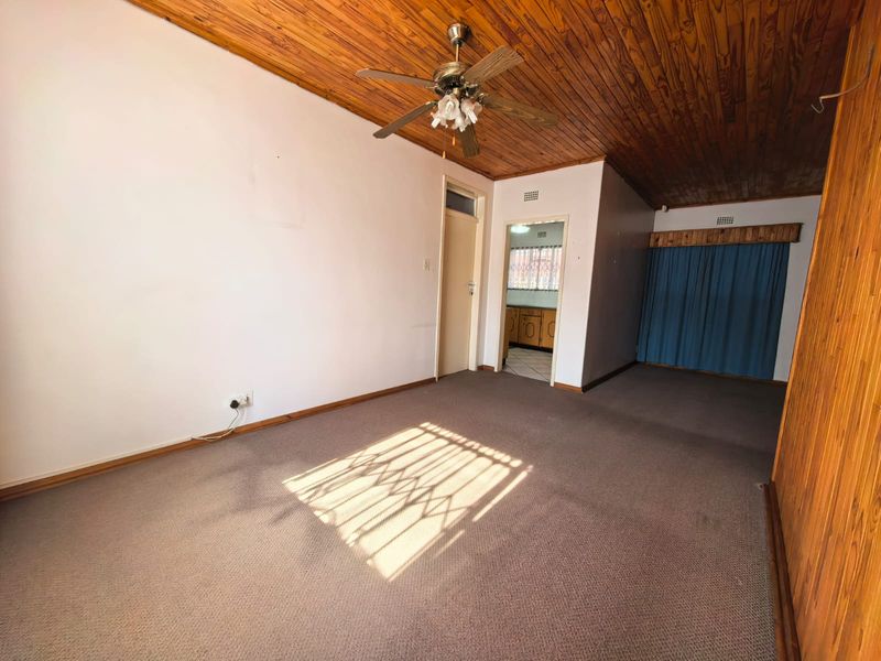 Spacious living area featuring timber ceiling paneling, a ceiling fan, and carpeted flooring, offering a blank canvas for renovation.