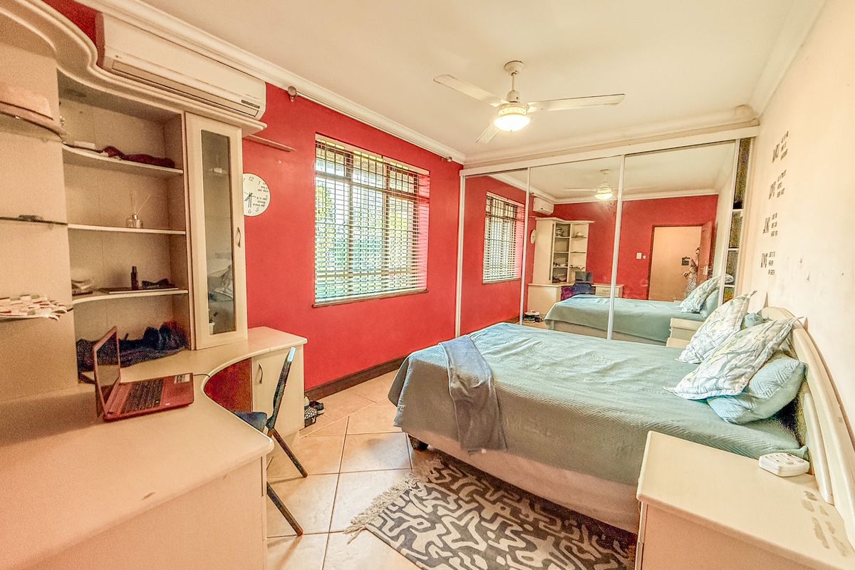 Spacious bedroom featuring built-in mirrored cupboards, ceiling fan, air conditioning, and tiled flooring, offering a functional layout with ample storage.