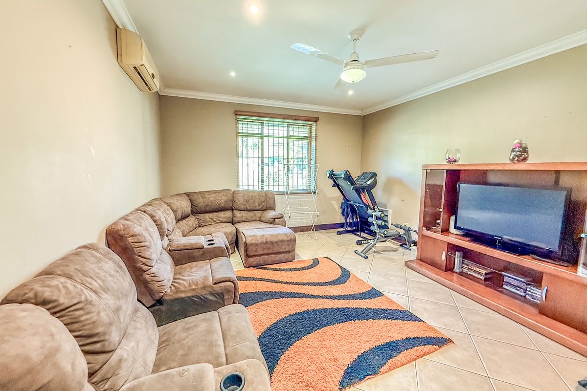 A spacious living room featuring tiled flooring, ceiling fan, and wall-mounted air conditioning unit, providing a functional and comfortable family living space.