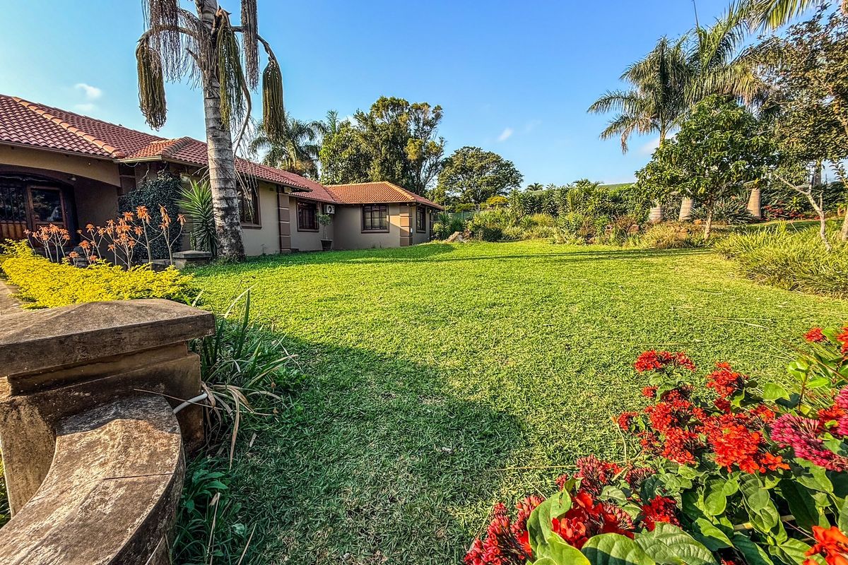 A spacious rear garden featuring a well-maintained lawn, mature trees, vibrant flower beds, and a built-in concrete bench, adjacent to the home's rear facade.